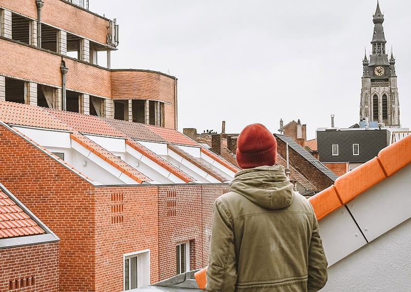 Projectbeeld Tuinstraat Kortrijk: gevelaanzicht van licht meergezinswoningenproject met geel-witte baksteen, witte stalen balkons en speelse tuinscene met spelende kinderen op de voorgrond - illustratieve rendering met zachte rozige sky.